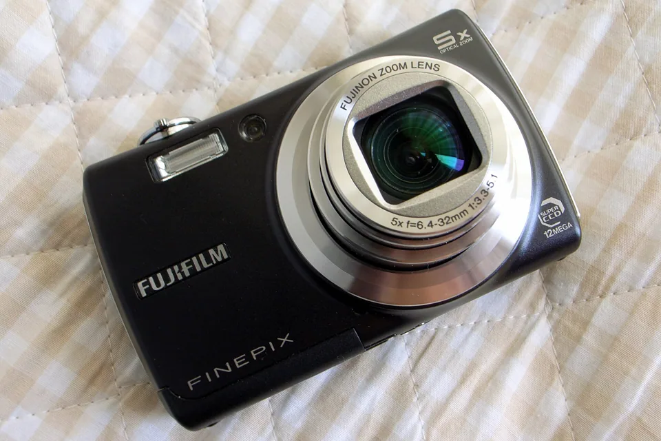 The Fujifilm FinePix F100fd in a dark finish, seen from the front with its 5x Fujinon lens.
