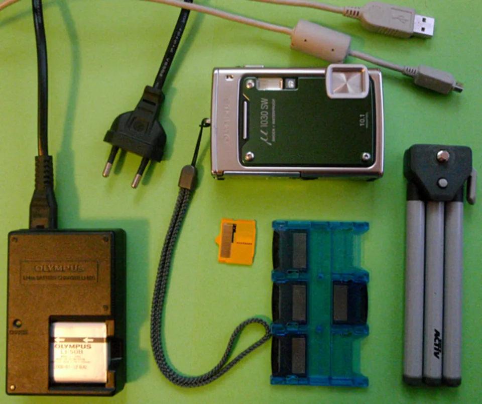 The Olympus µ 1030 SW (Stylus 1030 SW in the US) with its charger, strap, tripod and memory-card case.