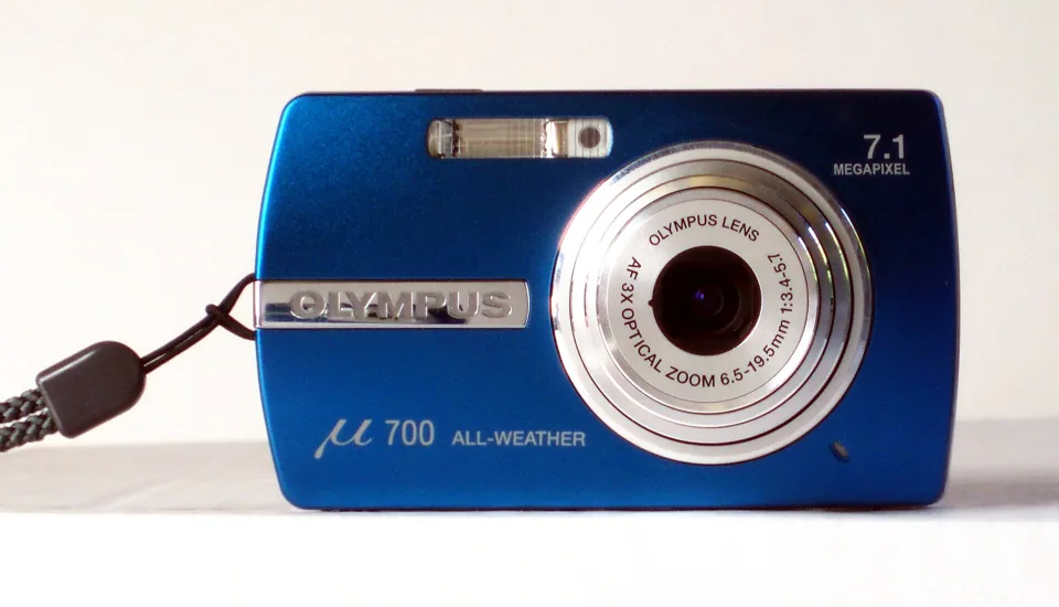 An Olympus µ 700 (Stylus 710), the blue version, seen from the front. The lens ring reads 6.5-19.5 mm, 1:3.4-5.7.